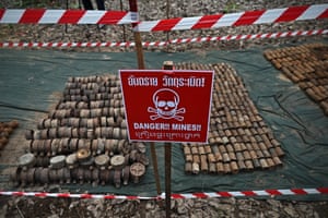 Dozens of landmines laid out in lines on the ground behind a large red skull-and-crossbones sign
