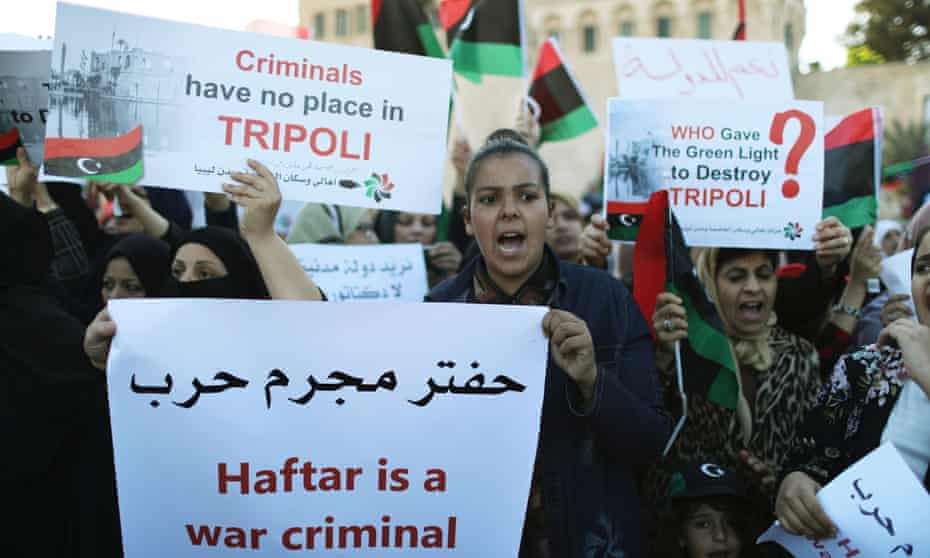 Women hold a poster with Arabic writing and English that reads "Haftar is a war criminal"