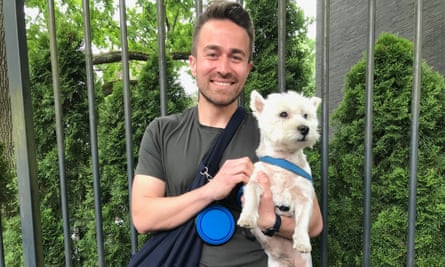 Young man in green T-shirt smiling and holding white scottish terrier