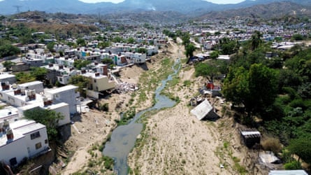 A stream runs along a sandy riverbed between suburban houses