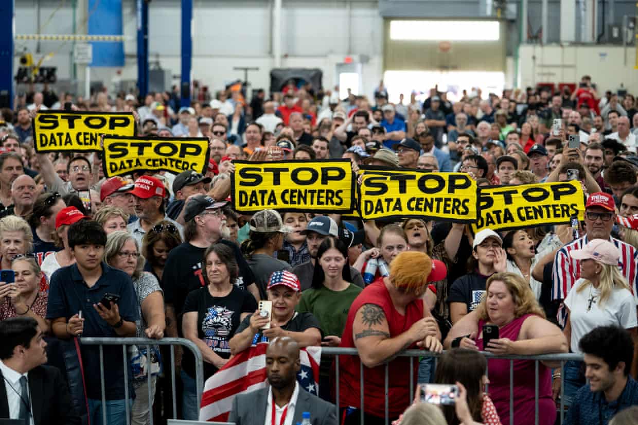 People in a crowd behind cattle guards hold up yellow and black signs that say “Stop Data Centers.”