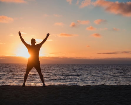 A man doing jumping jacks connected nan beach, looking retired towards nan oversea and nan sunset