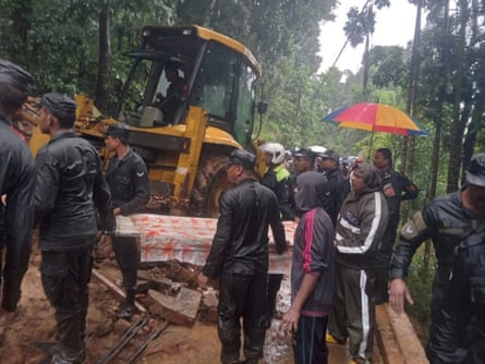 Rescue workers use a digger on a mountainside with people crowding around.