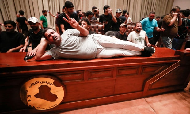 A supporter of Iraqi cleric Moqtada al-Sadr makes a victory symbol as he lies on the desk of the speaker of the Iraqi parliament.