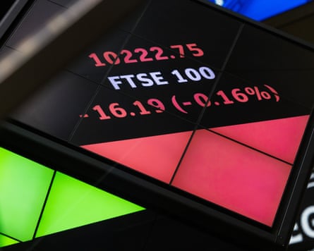 A digital board displays the FTSE 100 index figures in red text at the London Stock Exchange
