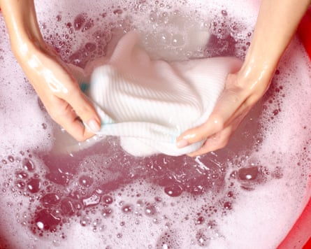 Women washing white sweater clothes in basin with powdered detergent, top view