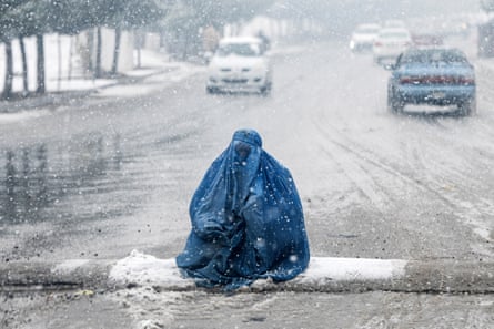 A person huddled in a blue burqa sits on a speed bump in the middle of a snowy main road