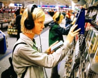 A young person wearing headphones examines a CD case in a shop aisle
