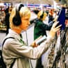 A young person wearing headphones examines a CD case in a shop aisle
