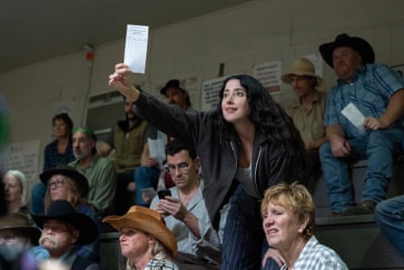 A woman in a crowd at a sport game holds up a piece of paper with her companion looking quizzically at this phone