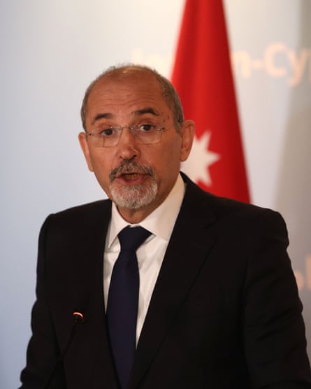 Ayman Safadi speaks at a summit. He has a short, neat grey beard and wears glasses. He is in a black jacket with white shirt and black tie.