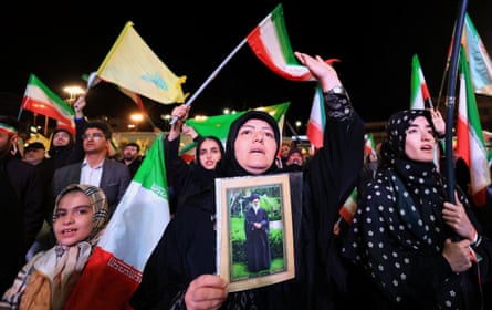 Women wearing hijabs wave Iranian flags and one holds up a photo of the former ayatollah