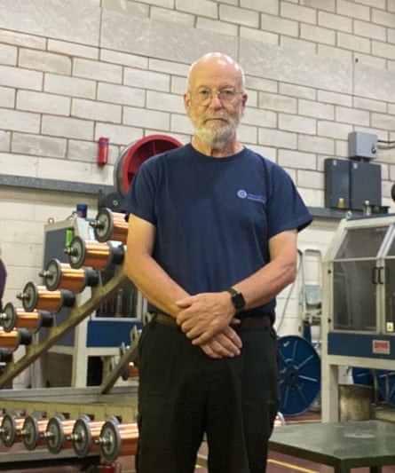 A man standing in a warehouse space surrounded by industrial machinery to make wires