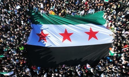 Syrians raise a giant independence-era flag, used by the opposition since the uprising began in 2011, as they celebrate the fall of Assad in Damascus.