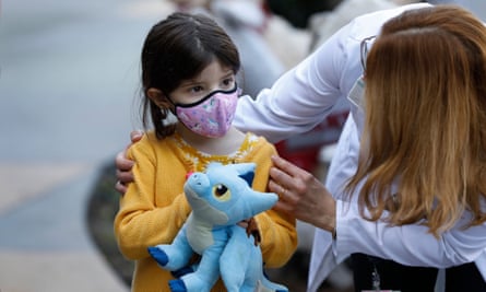 little girl clutching a blue stuffed toy being comforted by a doctor in a white coat
