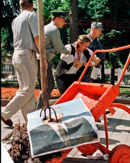 Ales Pushkin, wearing a headband and a waistcoat is led away by three men in uniform after he brought a wheelbarrow filled with manure and dumped it in front of Lukashenko’s office