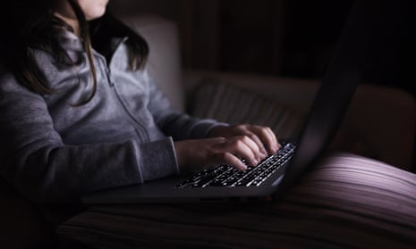 A girl sitting in a dark room and typing on a laptop