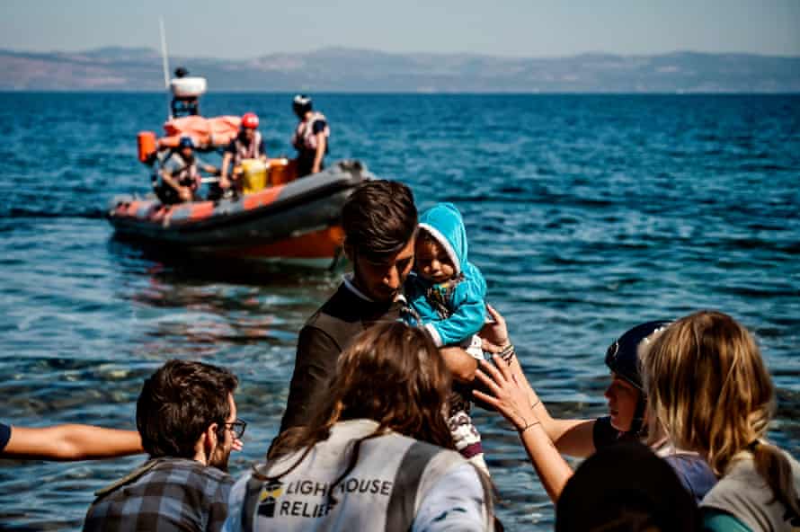 A migrant with a child is helped by rescuers as he arrives on the Greek island of Lesbos in September 2019.