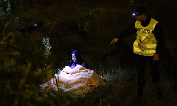 A woman and her five-year-old child (under blanket) are approached by a French police officer during a nightly patrol of the Eurotunnel perimeter fence in Calais.