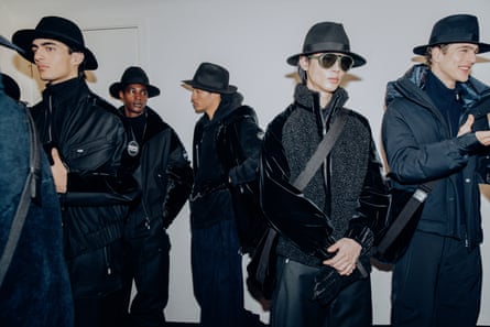 Models backstage wearing dark black coats and black stetson hats.