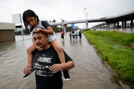 A man carries his young girl on his shoulders through a flooded street.