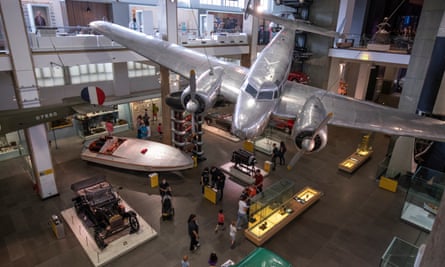 View of the Science Museum's transport display seen from above, with a vintage car and boat and a silver propeller plane suspended in mid-air from the ceiling