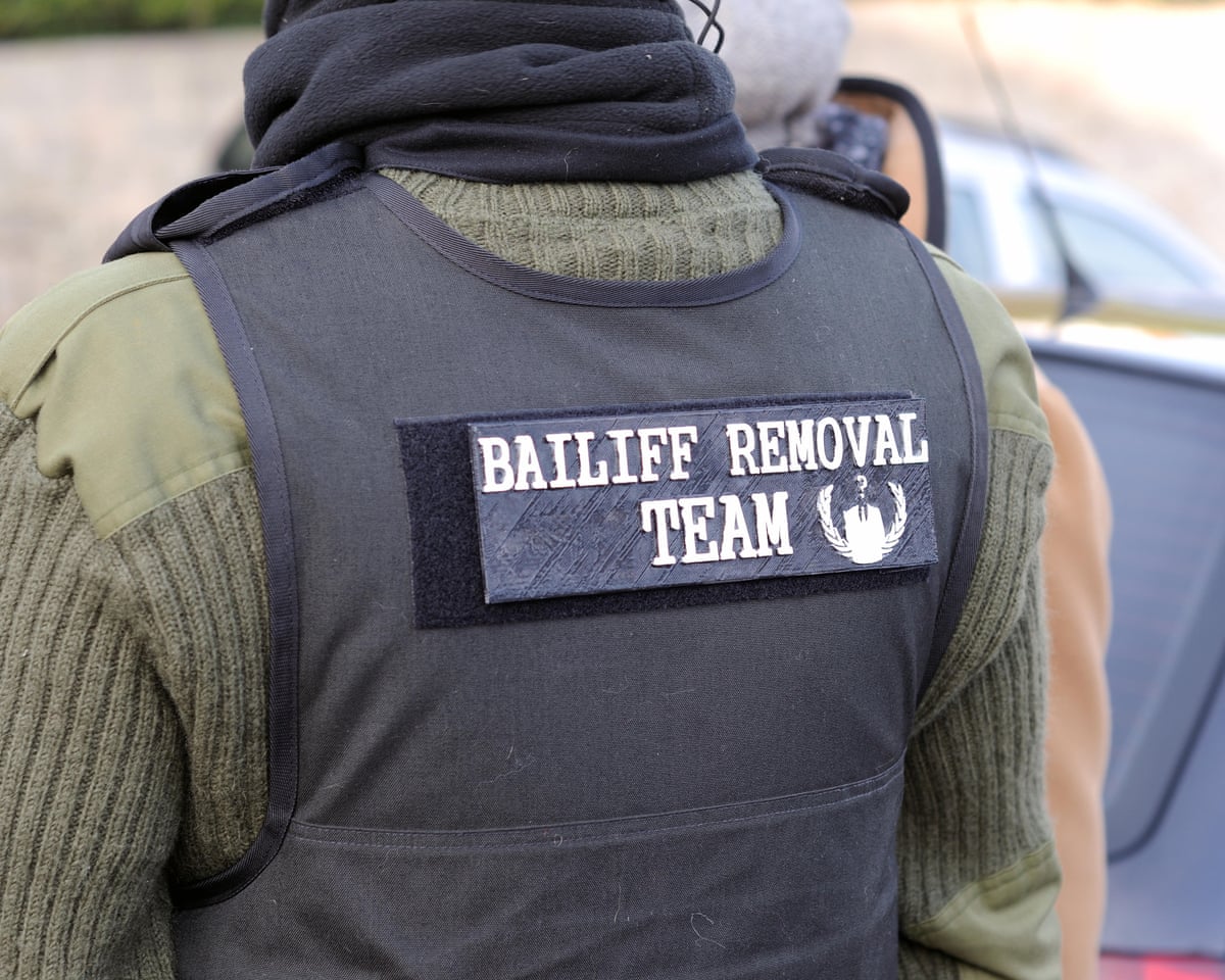 A bailiff seen from behind wearing a protective jacket