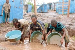 Using makeshift pans, children sluice gold ore while standing ankle deep in water