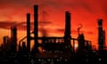 An oil refinery pictured in silhouette against an orange and red sunset