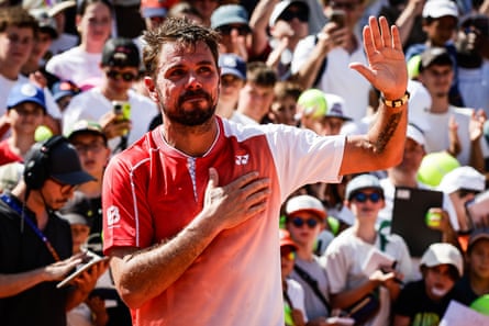 Stan Wawrinka in a red and white shirt places his hand on his chest and waves to the crowd