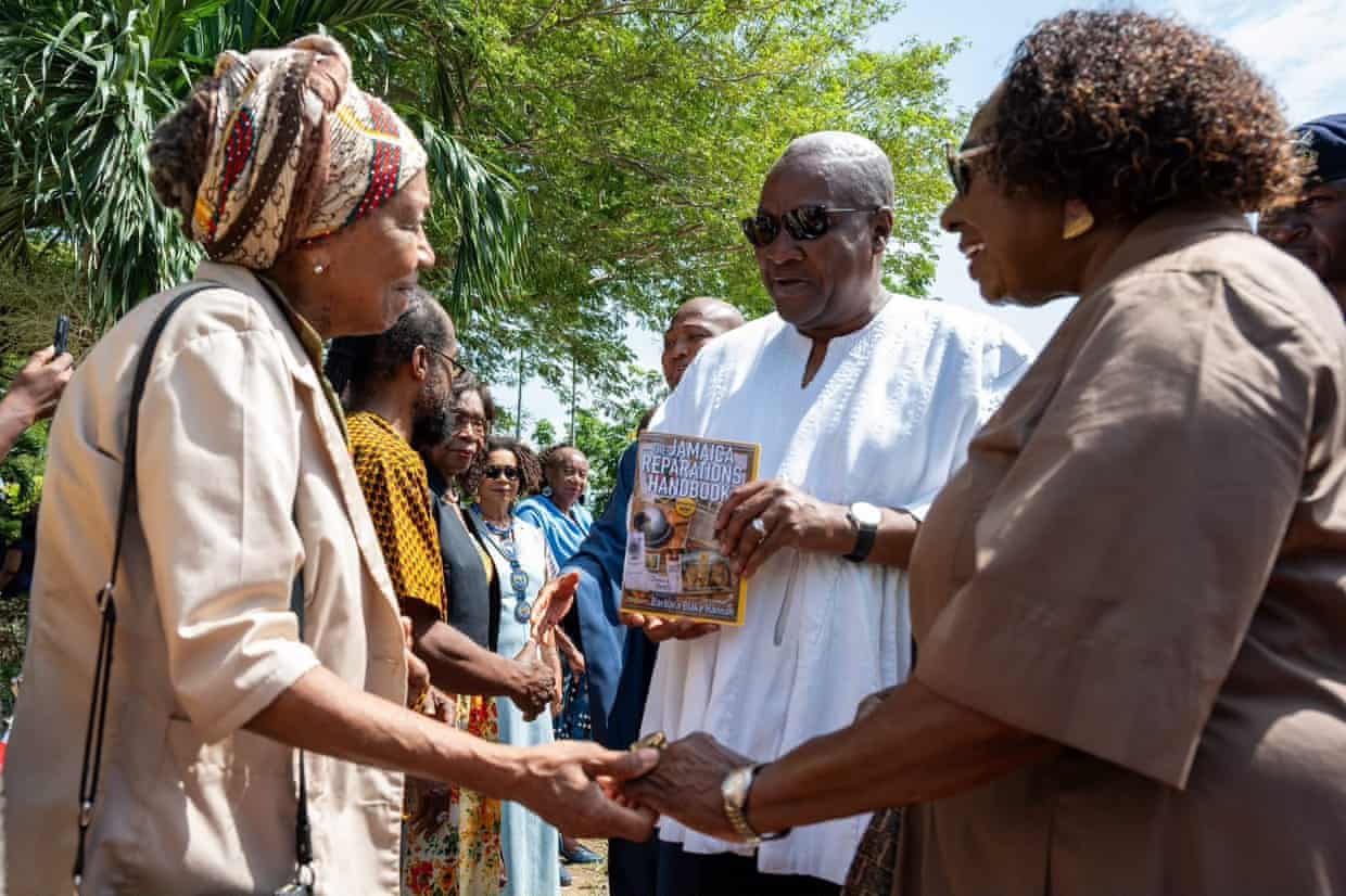 Barbara Blake Hannah holds the hand of Olivia Babsy Grange as John Dramani Mahama holds a book, The Jamaica Reparations Handbook