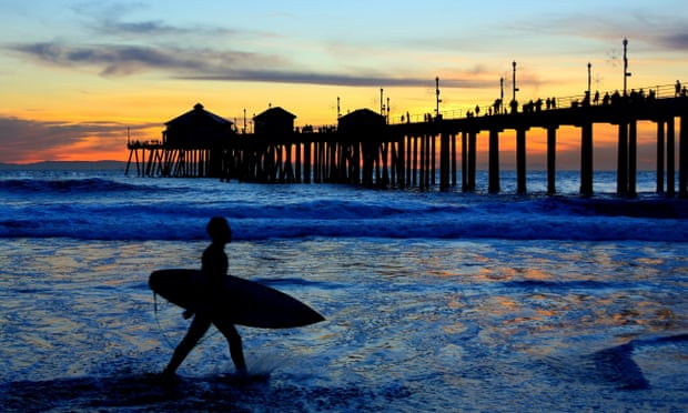 A surfer silhouetted against a beautiful California sunset and pier.