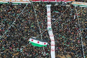 Idlib, Syria. People carry a giant Syrian opposition flag before it is hoisted on a mast during a rally to mark the 12th anniversary of the start of the uprising against the Syrian president, Bashar al-Assad, and his government in the rebel-held north-western city