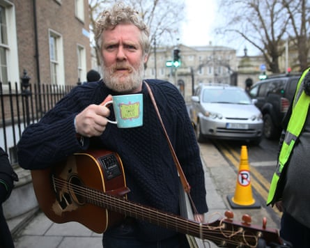 Glen Hansard outside with guitar and cup of tea