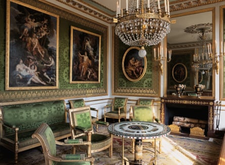 An ornate drawing room, featuring upholstered chairs and gold-framed art on the walls