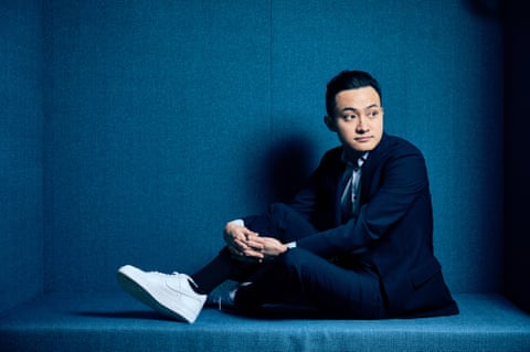 A man in a suit and sneakers posing while seated