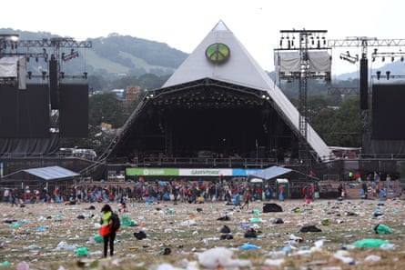 A cleaner collects litter that has strewn all over parched grass in front of the Pyramid stage in the aftermath of the Glastonbury festival 2023