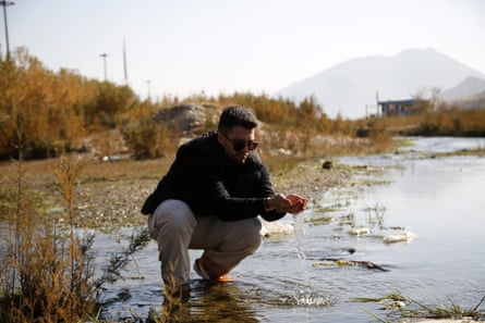 A man crouching down in an almost-dried-up river and cupping water in his hands