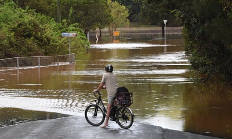 A person on a bike looks out over a flooded road in Lismore, New South Wales