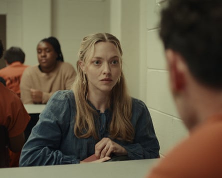 woman seated at table facing an inmate in orange uniform