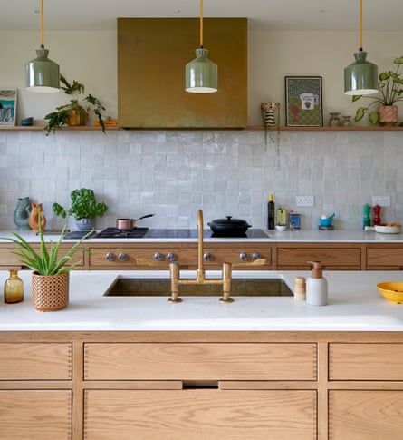 A kitchen with plain wooden drawer units, green pendant lights and a white stone worktop