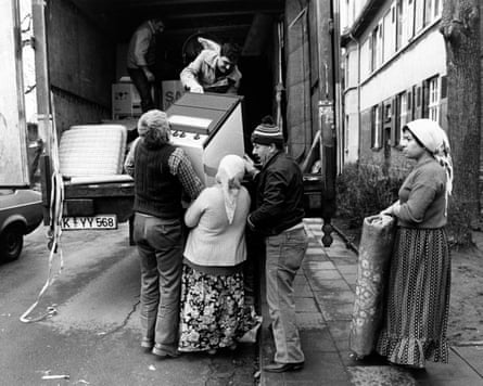 People load an oven and other furniture into a van. The women wear long skirts and headscarves