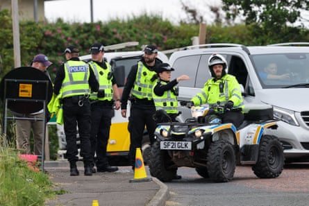Police stand on a footpath and on a road, and one sits on a quad bike