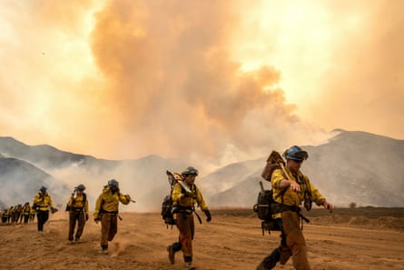 firefighters walk in a line as smoke billows in the background