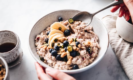 Hands hold a spoon and white bowl with oats, bananas and blueberries