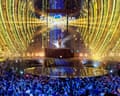 Loreen stands on a raised podium on stage under Eurovision branding as the crowd looks on