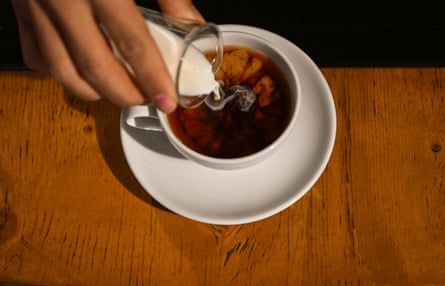 Milk being poured into a teacup of black tea, so the white milk blooms through the dark liquid.