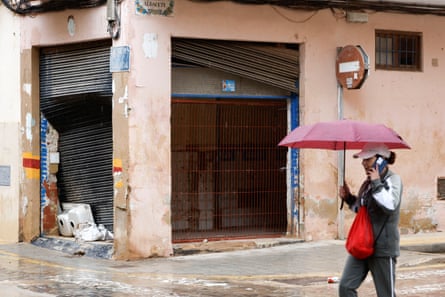 A pedestrian holding an umbrella walks past a building damaged by flooding