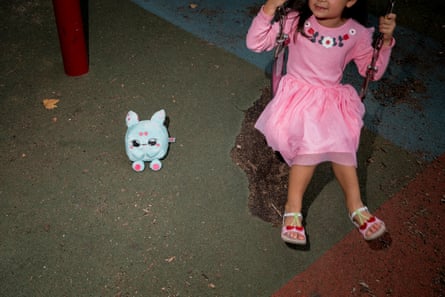 a child wearing a pink dress sits on a swing next to a blue plushy toy on the ground
