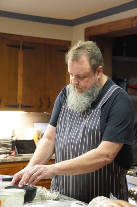 Man in long beard and chef’s apron works on a kitchen island.